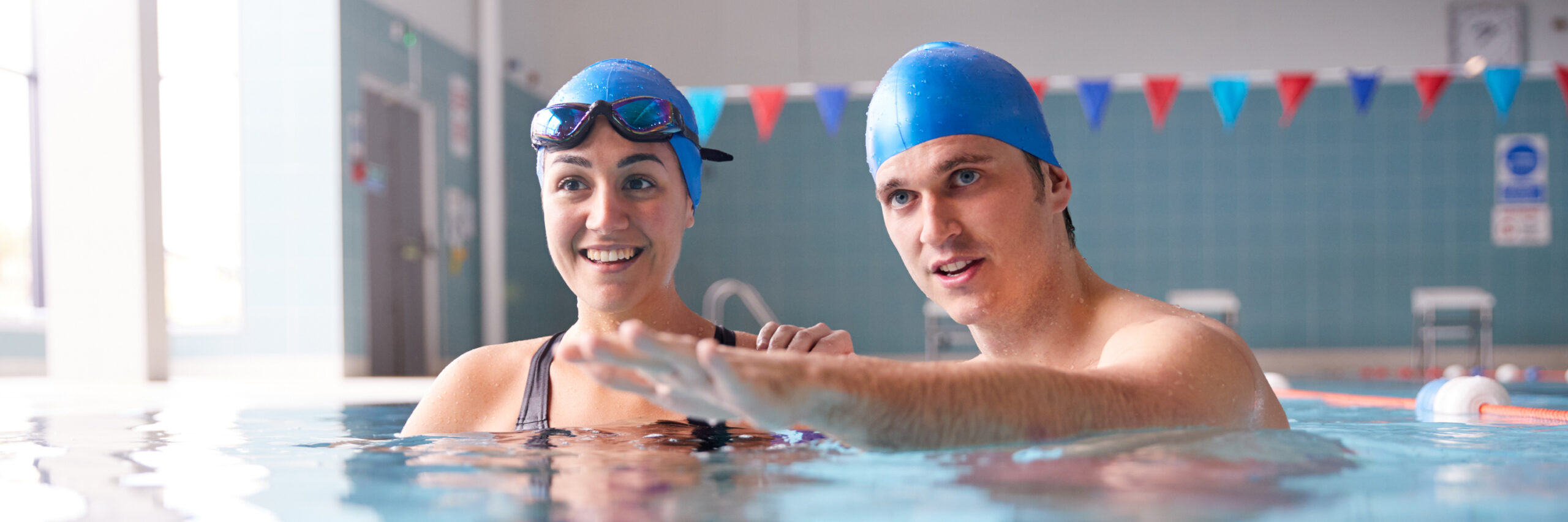 Male Swimming Teacher Giving Woman One To One Lesson In Pool